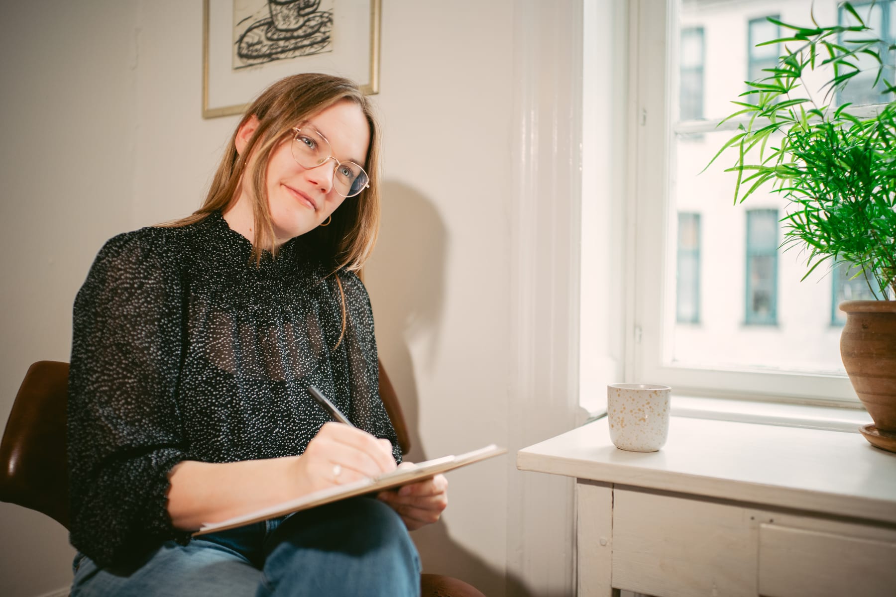Anna Langfred sidder i klinikken og tager noter, med en grøn plante i vinduet bagved
